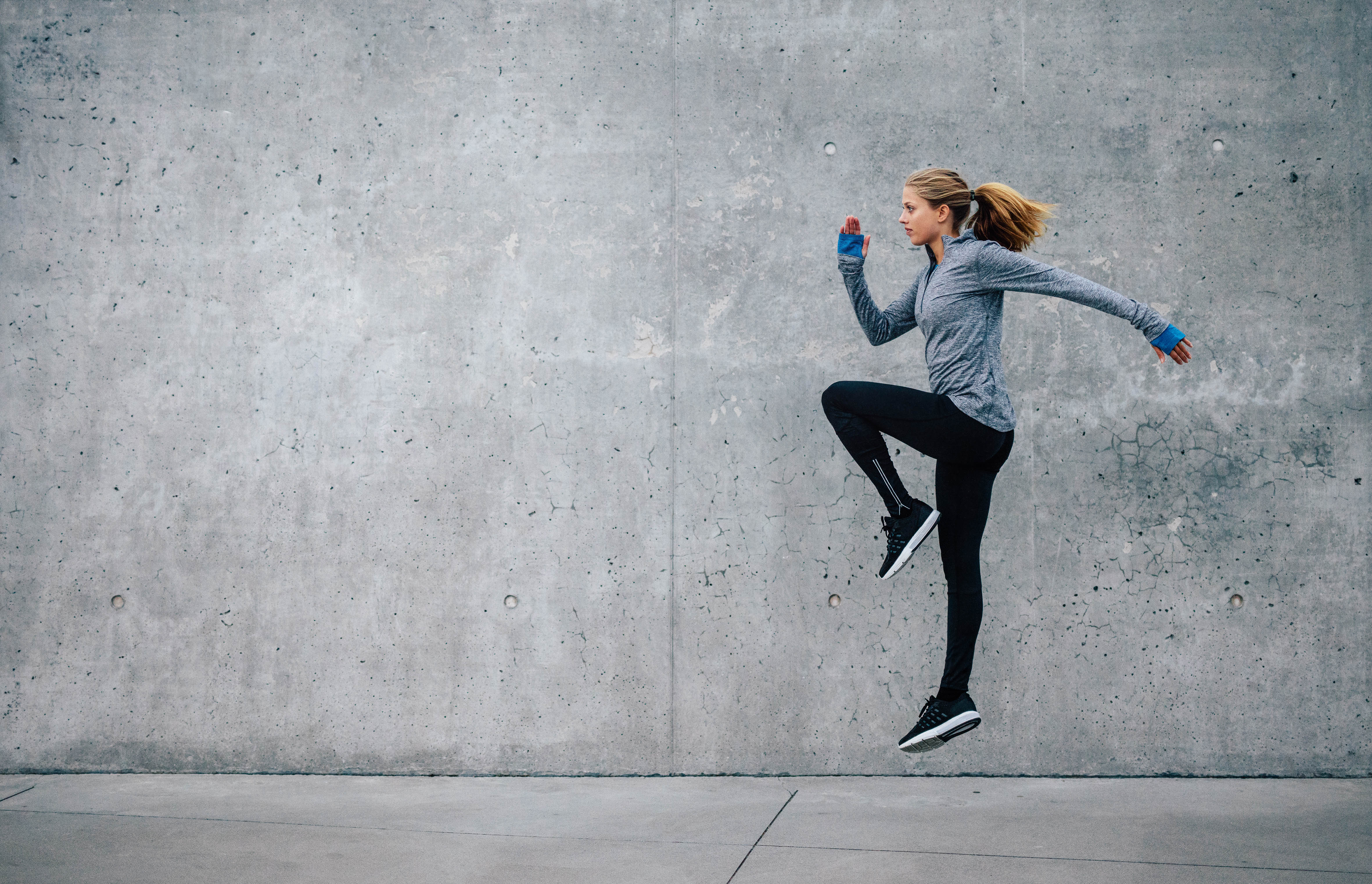 Young, fit woman doing vertical one legged jumps in front of a concrete wall